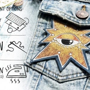 May include: A star-shaped patch with a central eye design attached to a light blue denim jacket pocket. Text reads: ATTACHMENT OPTIONS: VELCRO (HOOK & LOOP), SEW ON, IRON-ON (HEAT-ACTIVATED), accompanied by icons for each method.