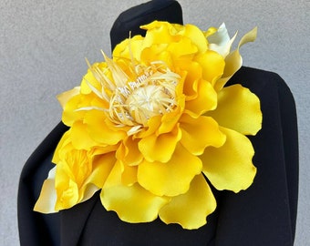 May include: A large, yellow silk flower with a textured center. The flower is attached to a black fabric background.