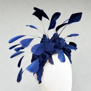 May include: A navy blue fabric flower with feathers arranged around it. The flower is on a white mannequin head.
