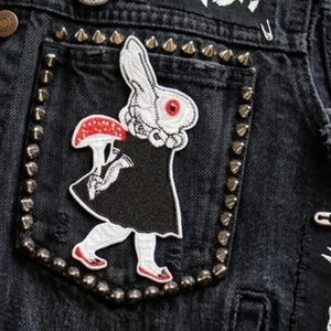 Puede incluir: Una taza de cerámica blanca con un asa negra y el texto "But First, Coffee" en negrita negra. La taza está sobre un fondo borroso. La taza mide aproximadamente 10 cm de altura.