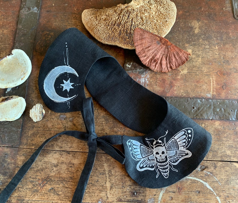 K&ouml;nnte beinhalten: Schwarzer Leinenkragen mit wei&szlig;er Stickerei eines Halbmondes, eines Sterns und eines Totenkopfschmetterlings. Der Kragen hat einen Bindeverschluss.