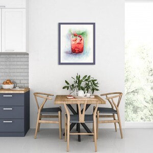 May include: A watercolor painting of a glass of red drink with ice and mint leaves. The painting is framed and hanging on a white wall in a dining room.