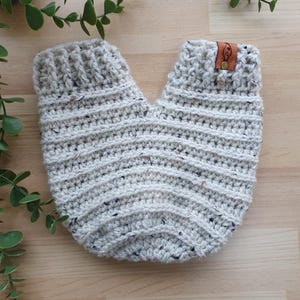 May include: A pair of beige crocheted baby booties with a brown leather tag that says "KC".