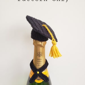 Könnte beinhalten: Ein schwarzes und gelbes Häkel-Set aus Abschluss-Kappe und Schal für eine Champagnerflasche. Die Kappe hat einen Quasten und der Schal einen gelben Knopf.