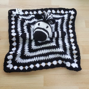 May include: Black and white crocheted baby blanket with a zebra-shaped stuffed animal in the center.