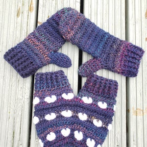 May include: A pair of crocheted fingerless gloves in a deep purple and blue colour with white hearts. The gloves are made with a textured yarn and have a unique design.