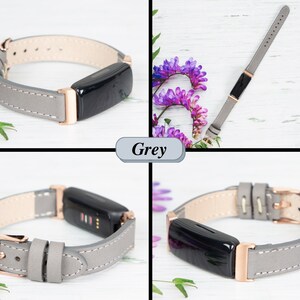 May include: A grey leather watch strap with rose gold hardware. The strap is shown on a white wooden surface with purple flowers.