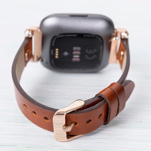 May include: A brown leather watch band with a rose gold buckle and a silver smartwatch face.