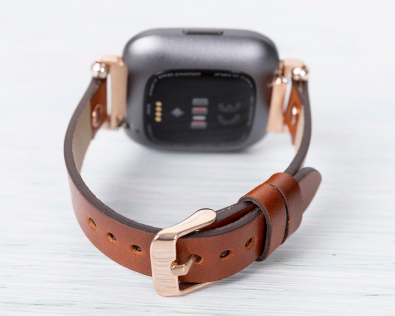 May include: A brown leather watch band with a rose gold buckle and a silver smartwatch face.