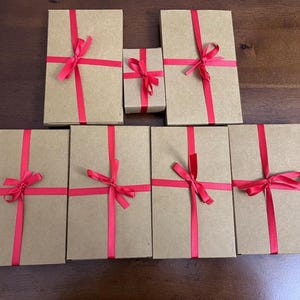 Puede incluir: Siete cajas de regalo marrones atadas con una cinta roja. Las cajas est&aacute;n dispuestas en dos filas, con la caja m&aacute;s peque&ntilde;a en el centro.