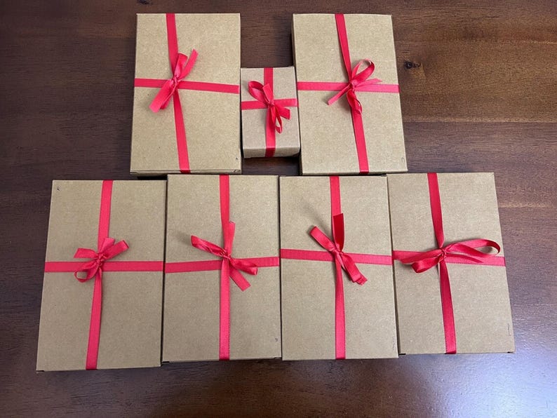 Puede incluir: Siete cajas de regalo marrones atadas con una cinta roja. Las cajas est&aacute;n dispuestas en dos filas, con la caja m&aacute;s peque&ntilde;a en el centro.
