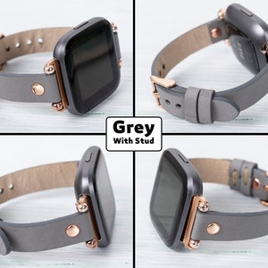 May include: A gray leather watch band with rose gold accents and studs. The band is compatible with a square-shaped smartwatch.