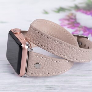 May include: A rose gold Apple Watch with a beige leather band. The band is double wrapped around the watch.