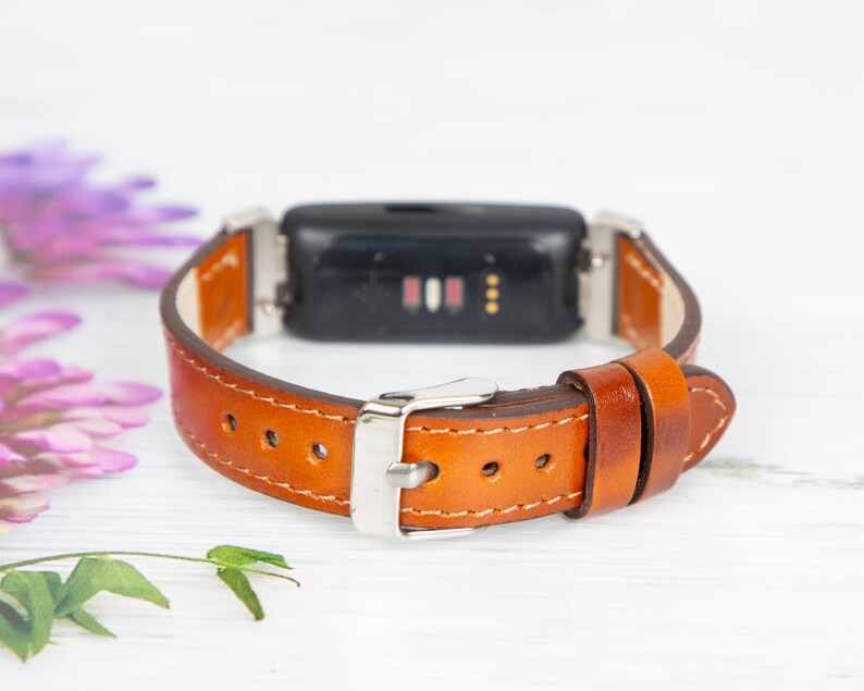 May include: A brown leather watch strap with a silver buckle. The strap is designed to fit a fitness tracker.