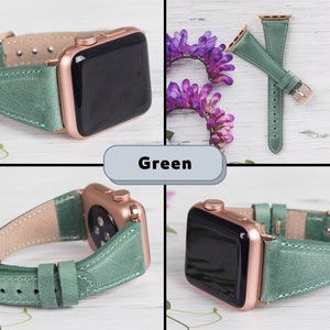 Puede incluir: Una correa de reloj de cuero verde para un Apple Watch con acabado en oro rosa. La correa se muestra sobre una superficie de madera blanca con flores moradas.