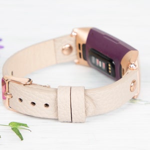 Puede incluir: Una banda de cuero beige con una hebilla de oro rosa y un rastreador de fitness morado. La banda est&aacute; dise&ntilde;ada para un reloj inteligente.
