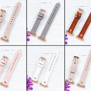 May include: Six pairs of watch bands in different colors and materials. The bands are shown on a white wooden background. The bands are all the same size and have a rose gold buckle.