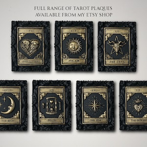 Pu&ograve; includere: Sette placche rettangolari da parete con disegni di carte dei tarocchi in nero e oro. Ogni placca ha una cornice nera decorata e un rilievo centrale dorato che raffigura simboli come Gli Amanti, Il Sole, Il Diavolo, La Luna, La Morte, La Stella e L'Imperatrice.
