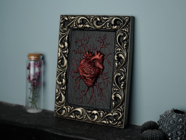 Peut inclure: Un c&oelig;ur anatomique encadr&eacute; avec des veines rouges sur un fond noir. Le cadre est orn&eacute; et argent&eacute; avec une patine sombre.