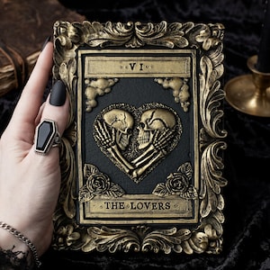 Pu&ograve; includere: Una placca rettangolare con un rilievo di due teschi che formano un cuore, etichettata VI e THE LOVERS. Il pezzo ha un centro nero e una cornice dorata ornata e anticata con accenti floreali. Un anello a forma di bara con una pietra nera.