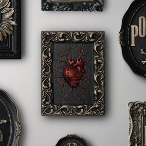 Peut inclure: Une collection d'&oelig;uvres d'art murales encadr&eacute;es sur le th&egrave;me gothique et macabre. Les cadres sont noirs et dor&eacute;s avec des d&eacute;tails orn&eacute;s. Les &oelig;uvres d'art comprennent un cr&acirc;ne avec un tournesol, un c&oelig;ur avec des veines, un cr&acirc;ne avec des os crois&eacute;s et le mot "Poison", et un fant&ocirc;me avec le mot "Big".