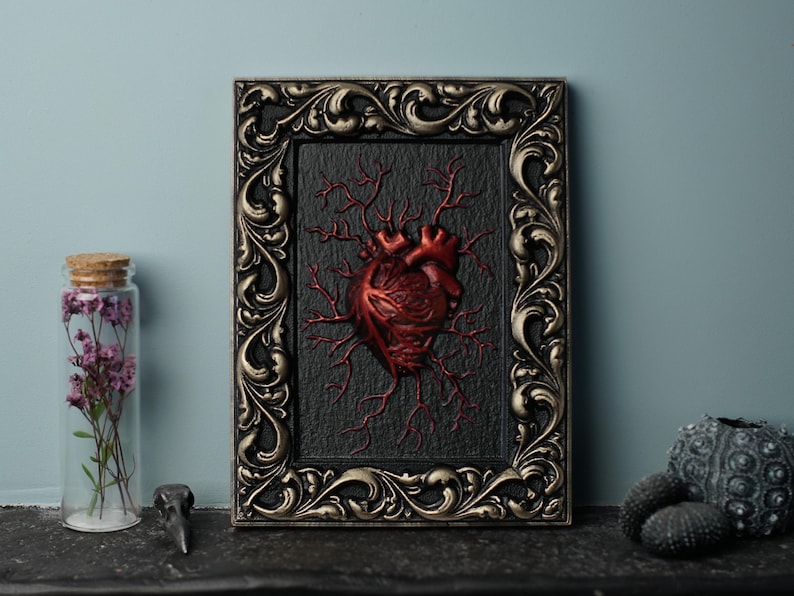 Peut inclure: Un c&oelig;ur anatomique encadr&eacute; avec des veines rouges sur un fond noir. Le cadre est orn&eacute; et dor&eacute;.