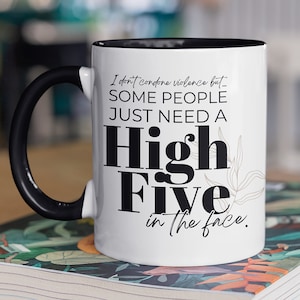 May include: White ceramic coffee mug with a black handle and black rim. The mug has a funny saying printed on it: "I don't condone violence but... SOME PEOPLE JUST NEED A High Five in the face."