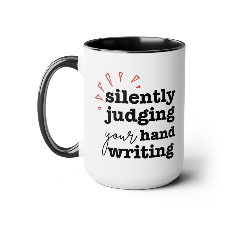 May include: White ceramic mug with a black handle and interior. The mug features the text "silently judging your hand writing" in black, with red accents.