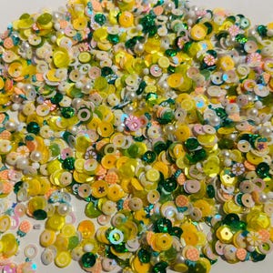 May include: A mix of yellow, green, and white sequins in various shapes and sizes. The sequins are perfect for crafting and decorating.