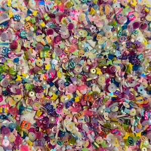 May include: A large assortment of colorful, mixed-media embellishments, including plastic, metal, and pearl-like beads, in various shapes and sizes. The embellishments are perfect for crafting and adding a touch of whimsy to projects.