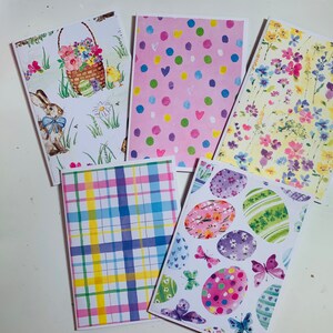 May include: Set of five Easter-themed greeting cards featuring different designs. One card has a pink background with colorful polka dots, another has a plaid pattern, and another has a floral design. The remaining two cards feature Easter eggs and bunnies.