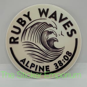 May include: A white round sticker with black text and a black and white wave design. The text reads "Ruby Waves Alpine 38:08".