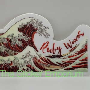 May include: A sticker featuring a stylized wave design in shades of red and white, with the words "Ruby Waves" in red script. The sticker has a white border and the text "The Sticker Emporium" in green.