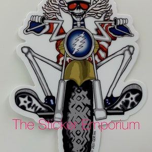 May include: A sticker featuring a skeleton riding a motorcycle, dressed in patriotic attire. The skeleton wears a red, white, and blue Uncle Sam hat and sunglasses. The motorcycle has a blue and gold emblem. The sticker has the text "The Sticker Emporium".