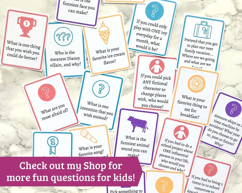 May include: A set of colorful cards with questions for kids. The cards are on a white marble surface. The questions are about favorite things, fictional characters, and funny sounds. The text on the cards includes "What is your favorite ice cream flavor?" and "What is the funniest animal sound you can make?"
