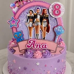 May include: A round purple cake decorated with small stars and sprinkles, topped with a large circular topper featuring three animated characters, a blue cat, a light stick, a number 8, and a pink banner with the name Ana printed in white.