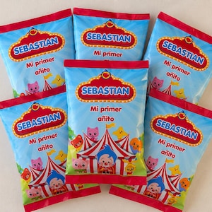 May include: Six blue party favor bags with red trim. Each bag features the name "SEBASTIAN" in a gold and red marquee design. Below the name is the text "Mi primer a&ntilde;ito" and a circus-themed illustration.