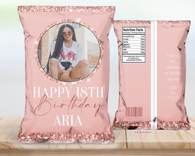 Puede incluir: Bolsa de patatas fritas rosa con detalles de purpurina oro rosa. La parte delantera presenta una foto dentro de un c&iacute;rculo, con el texto "HAPPY 18TH BIRTHDAY ARIA". La parte trasera incluye una tabla de informaci&oacute;n nutricional y un mensaje de agradecimiento.