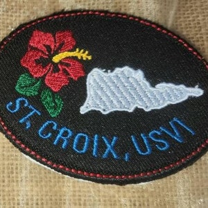 May include: Two embroidered patches with the text "St. Croix, USVI". The first patch features a yellow outline of the island of St. Croix with a palm tree. The second patch features a white outline of the island with a red hibiscus flower.