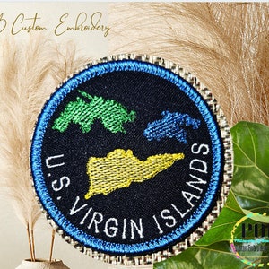 May include: Embroidered patch with a blue border, depicting the outline of the US Virgin Islands in green, blue, and yellow on a black background. The text "U.S. VIRGIN ISLANDS" is written in white around the islands.