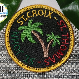May include: A round black embroidered patch with a yellow border. The patch features two palm trees with green leaves and brown trunks. The text "ST. CROIX - ST. THOMAS" is embroidered in red and green around the palm trees.