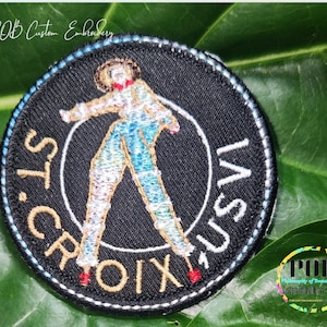 May include: A black and gold embroidered patch with a stylised figure and the text "ST. CROIX GUSV".