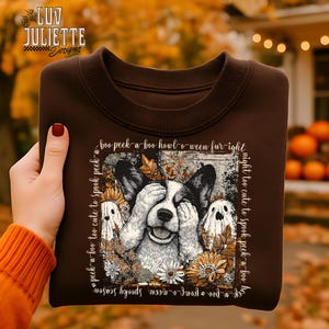 Może przedstawiać: Brązowa bluza z nadrukiem przedstawiającym psa zakrywającego oczy, otoczonego duchami i jesiennymi liśćmi. Projekt zawiera frazy "boo peek-a-boo howl-o-ween fur-ight" i "night too cute to spook peek-a-boo".