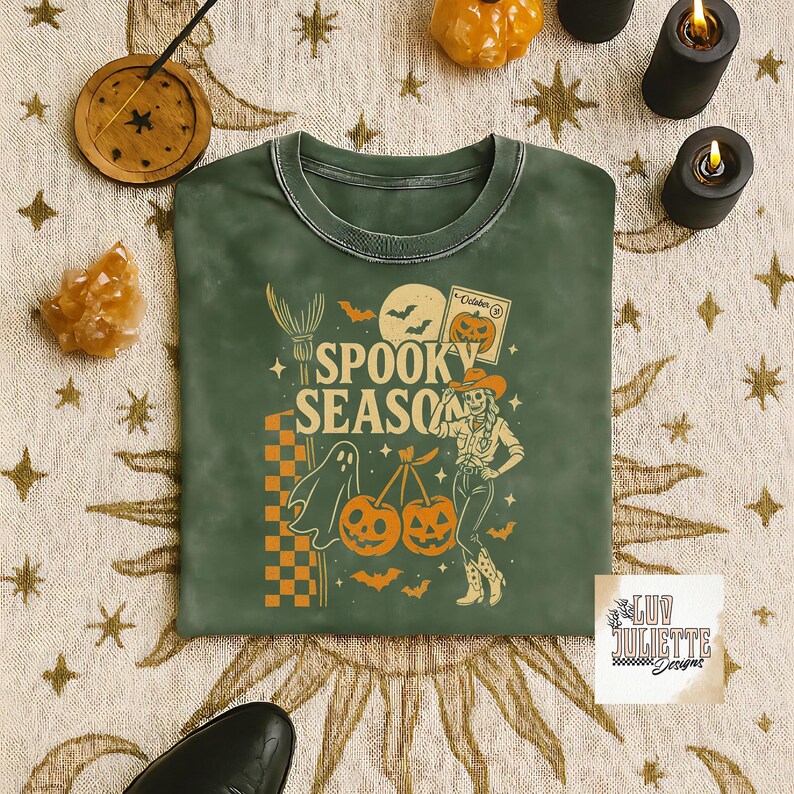 May include: Green crew neck sweatshirt with a Halloween-themed graphic. The design includes the words "Spooky Season", a ghost, pumpkins, bats, and a cowgirl. The sweatshirt has a vintage, washed look.