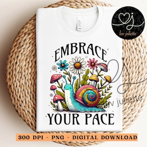 Puede incluir: Camiseta blanca con un gráfico colorido de caracol y flores. El texto "Embrace Your Pace" está impreso en negro en la camiseta.