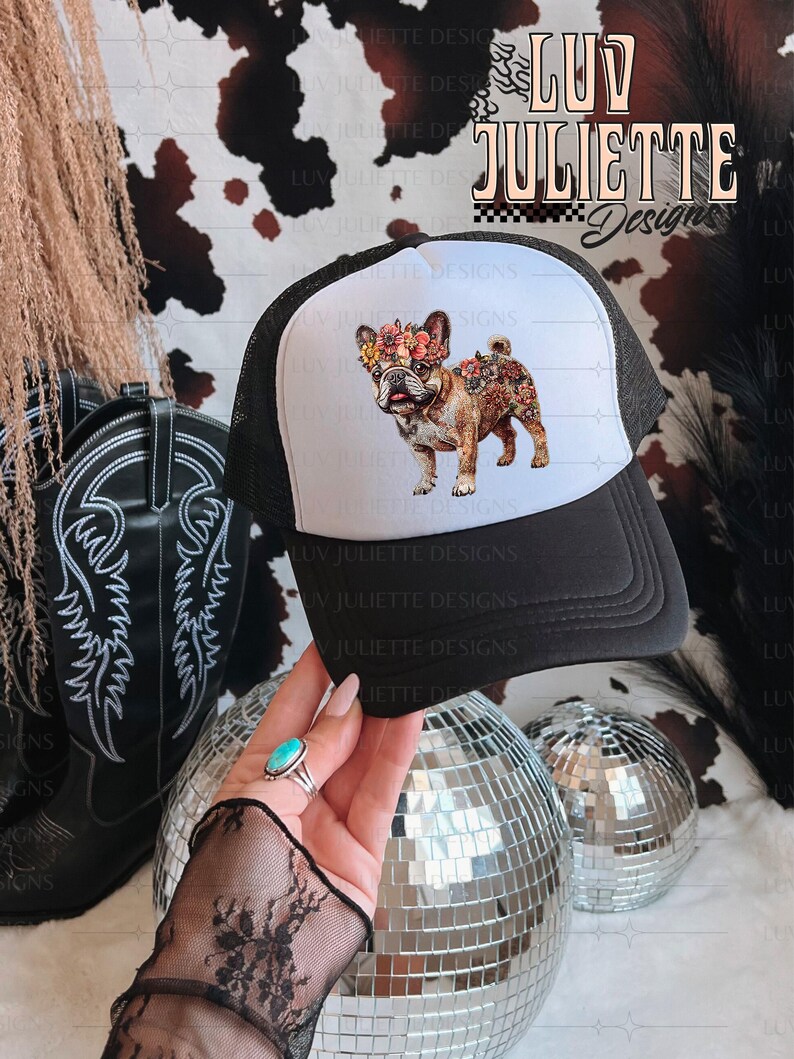 Puede incluir: Una gorra de camionero blanca y negra con un dise&ntilde;o floral en la parte delantera. El dise&ntilde;o presenta un bulldog franc&eacute;s con flores en la cabeza. El texto "LUV JULIETTE Design" es visible en la gorra.