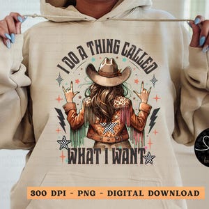 May include: Beige hoodie with a graphic of a woman in a cowboy hat and jacket, with the text "I DO A THING CALLED WHAT I WANT". The design includes stars, lightning bolts, and a heart logo.