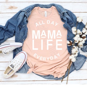 May include: A peach-colored t-shirt with the text "ALL DAY MAMA LIFE EVERYDAY" in white lettering.