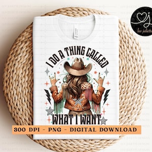 May include: White t-shirt with a graphic of a woman wearing a cowboy hat and jacket, with the text "I DO A THING CALLED WHAT I WANT." The design includes stars, lightning bolts, and a rock-on hand gesture. The shirt is displayed on a woven surface.