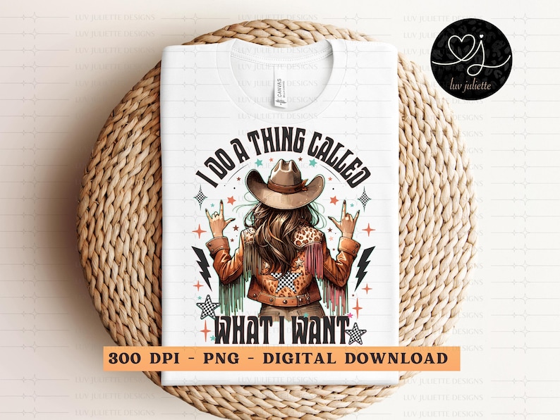 May include: White t-shirt with a graphic of a woman wearing a cowboy hat and jacket, with the text "I DO A THING CALLED WHAT I WANT." The design includes stars, lightning bolts, and a rock-on hand gesture. The shirt is displayed on a woven surface.